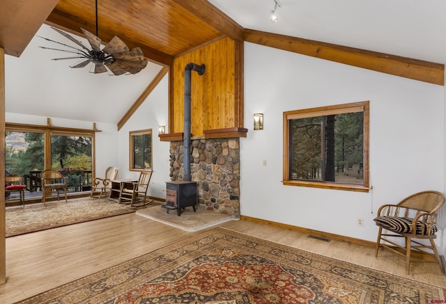 living area featuring lofted ceiling with beams, a wood stove, visible vents, ceiling fan, and wood finished floors