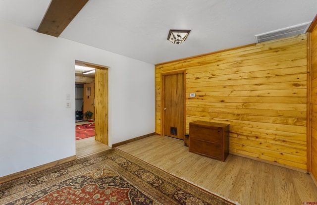 spare room featuring beam ceiling, wood walls, and light hardwood / wood-style flooring