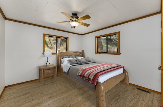 bedroom featuring visible vents, baseboards, ornamental molding, a ceiling fan, and wood finished floors