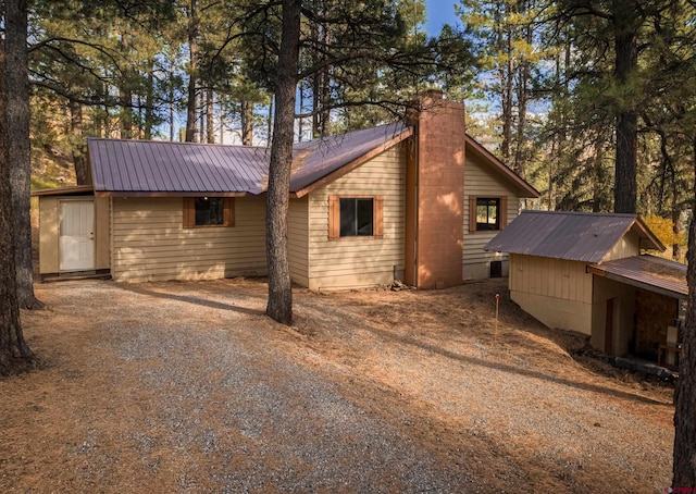 view of side of property featuring metal roof, driveway, and a chimney