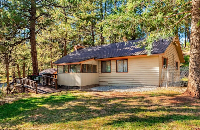 back of property featuring a wooden deck, metal roof, and a lawn