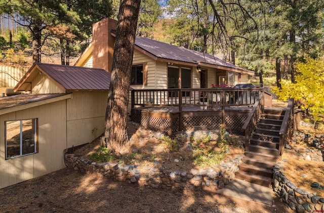 back of house featuring stairway, a deck, metal roof, and a chimney