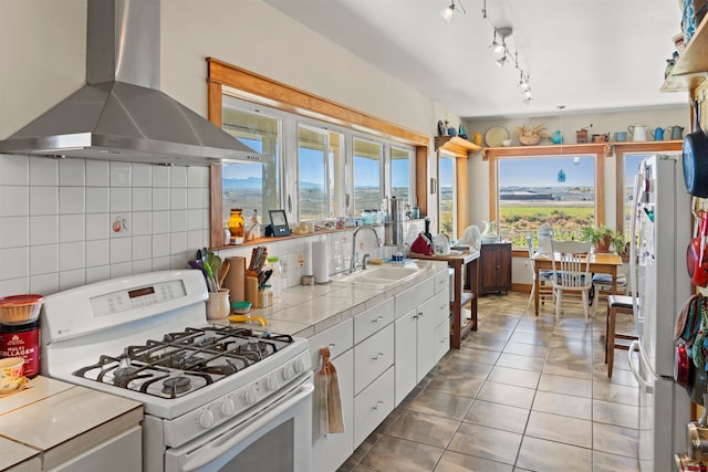 kitchen with white appliances, sink, tile countertops, white cabinetry, and wall chimney exhaust hood