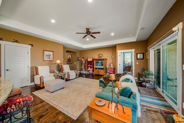 living room with a raised ceiling, dark hardwood / wood-style floors, and ceiling fan