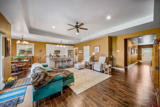 living room with ceiling fan with notable chandelier, a raised ceiling, and dark hardwood / wood-style flooring