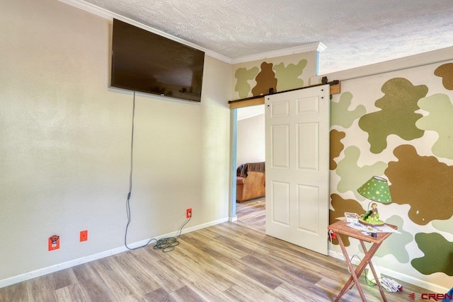 empty room with crown molding, a textured ceiling, hardwood / wood-style flooring, and a barn door