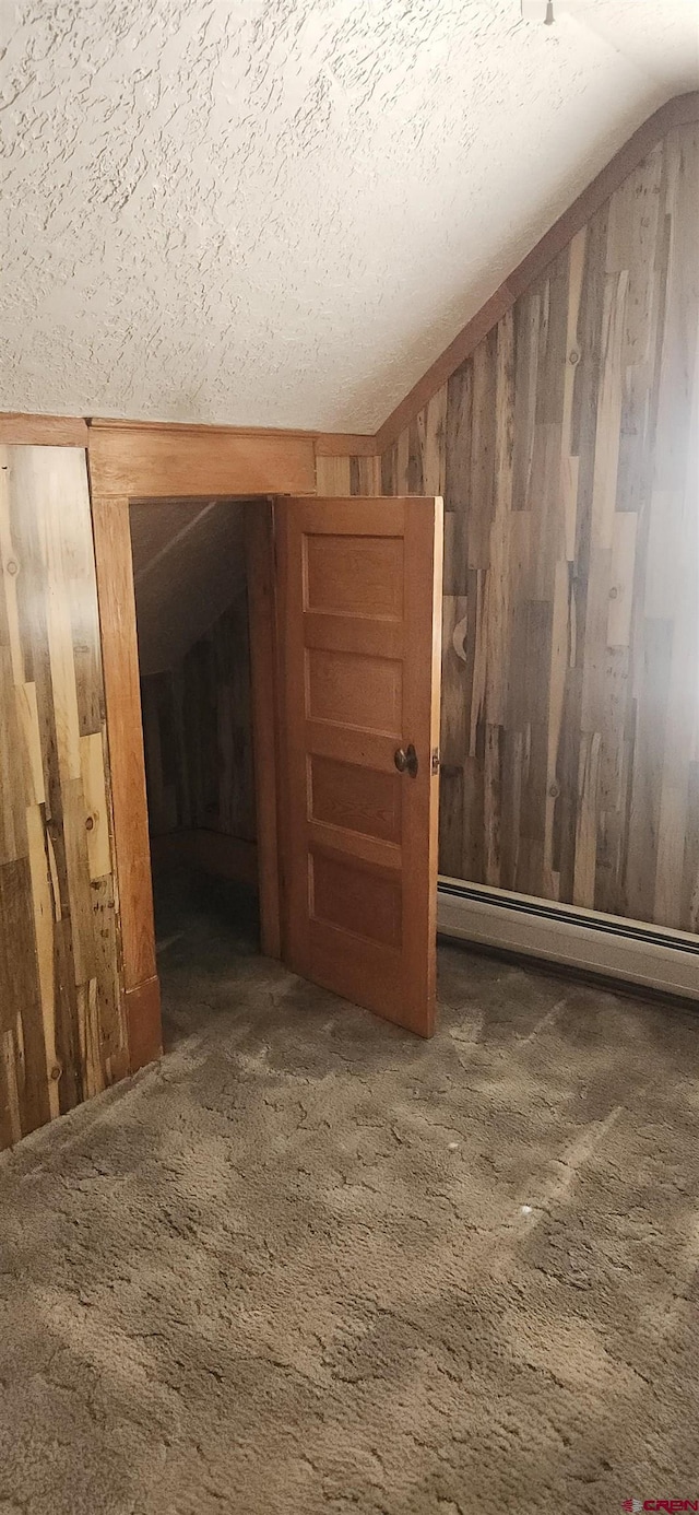 carpeted spare room with baseboard heating, lofted ceiling, wooden walls, and a textured ceiling