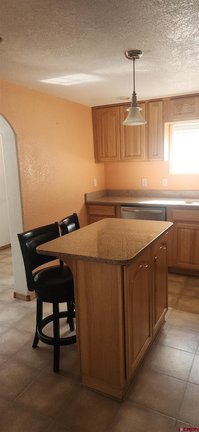 kitchen featuring hanging light fixtures, a kitchen island, a textured ceiling, a kitchen bar, and dishwasher