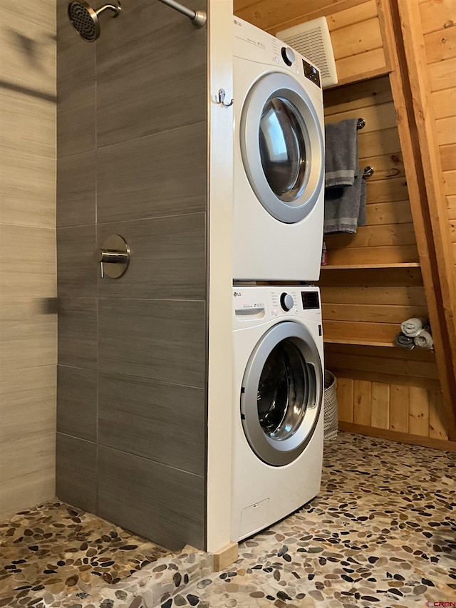 washroom with stacked washing maching and dryer and wooden walls