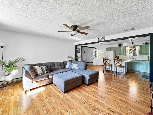 living room featuring light wood-type flooring, ceiling fan, and a textured ceiling