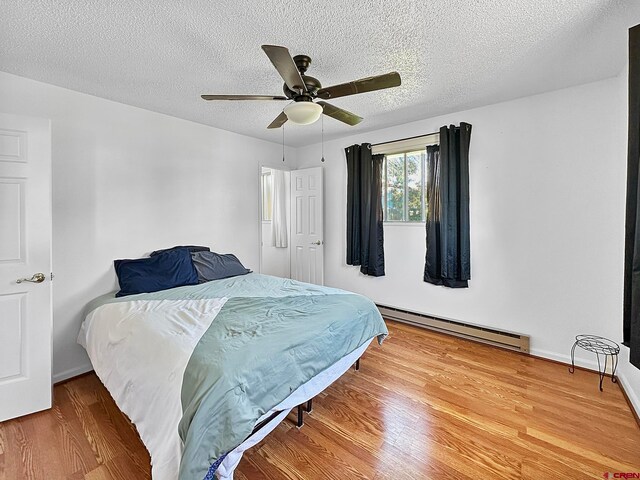 bedroom with ceiling fan, a baseboard radiator, a textured ceiling, and wood-type flooring