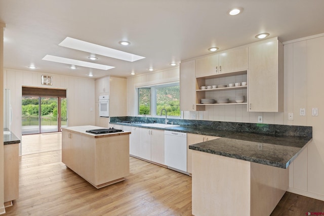 kitchen with a center island, white appliances, sink, light hardwood / wood-style floors, and dark stone counters