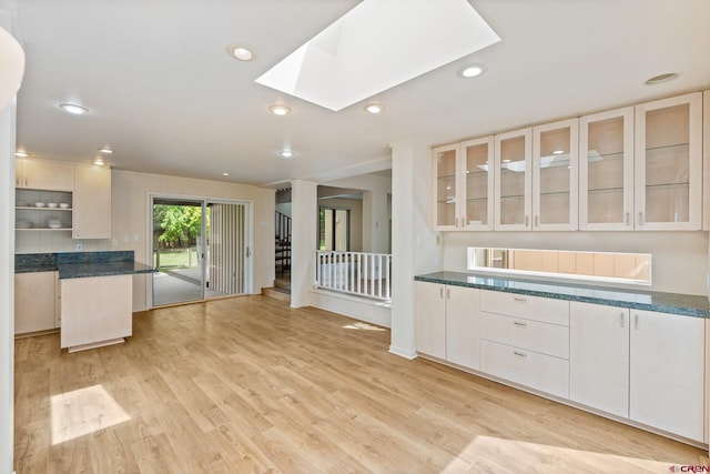 kitchen featuring white cabinets, a skylight, light hardwood / wood-style flooring, and dark stone counters