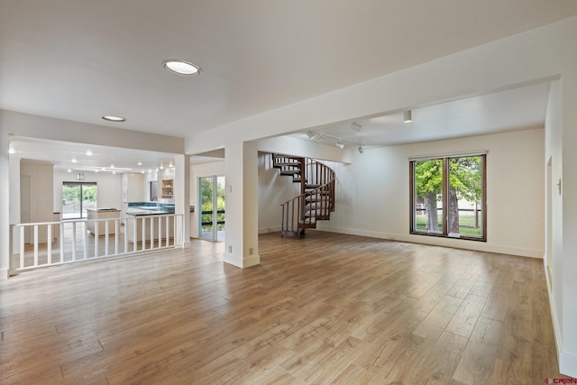 unfurnished living room with plenty of natural light, light hardwood / wood-style floors, and rail lighting