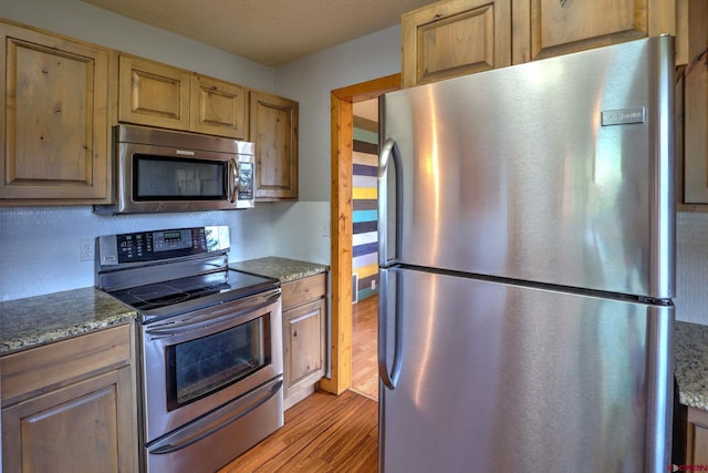 kitchen with dark stone countertops, light hardwood / wood-style floors, stainless steel appliances, and a textured ceiling