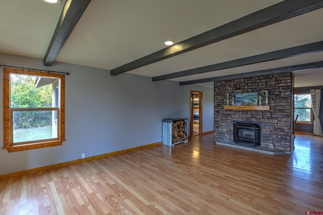 unfurnished living room with light wood-type flooring, beam ceiling, a wood stove, and a wealth of natural light