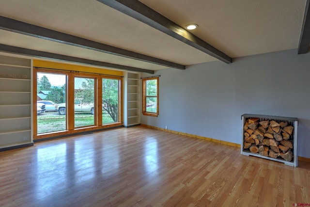 unfurnished living room featuring beamed ceiling, light hardwood / wood-style floors, and a textured ceiling