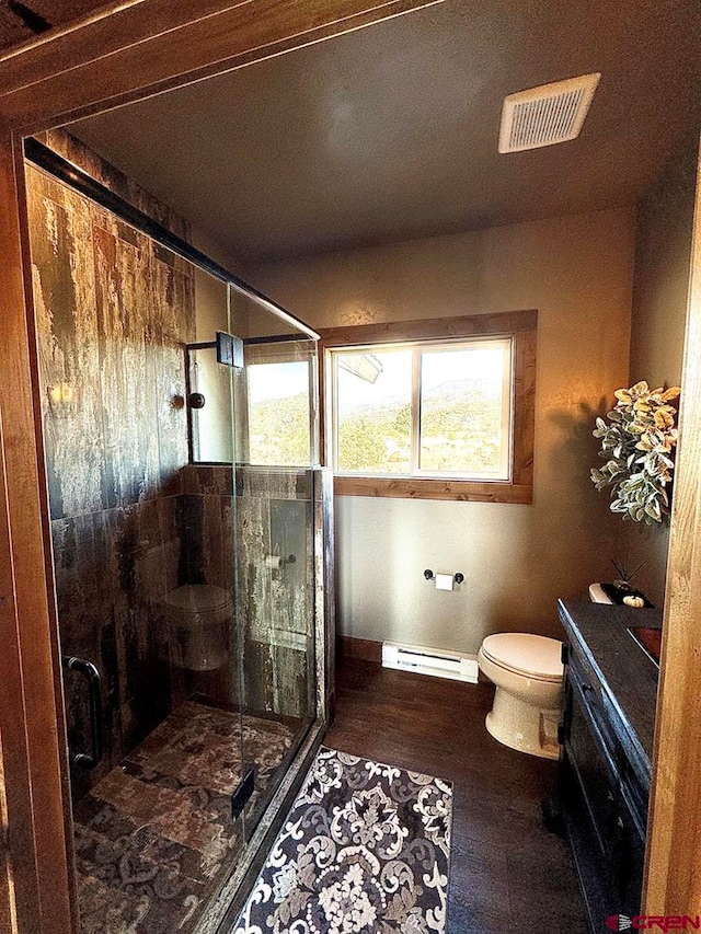 bathroom featuring vanity, wood-type flooring, an enclosed shower, a baseboard radiator, and toilet