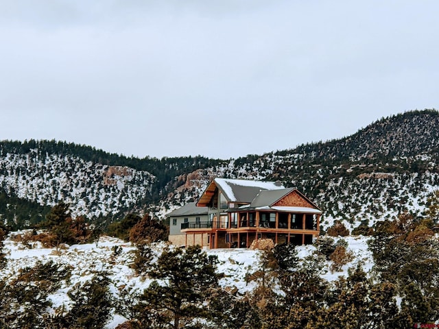 snow covered house with a deck with mountain view