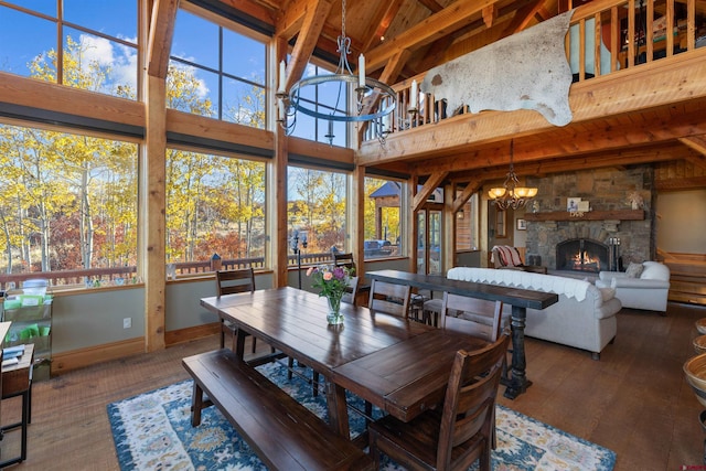 dining room featuring beamed ceiling, a stone fireplace, high vaulted ceiling, a notable chandelier, and dark hardwood / wood-style flooring