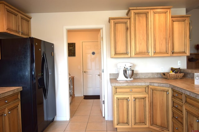 kitchen with light tile patterned floors, black refrigerator with ice dispenser, and washing machine and clothes dryer