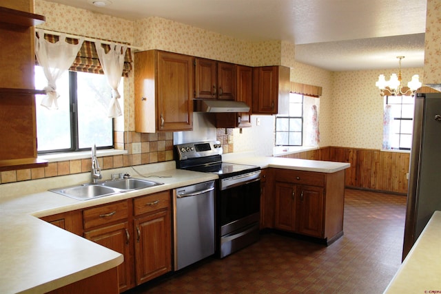 kitchen with appliances with stainless steel finishes, wooden walls, sink, decorative light fixtures, and plenty of natural light