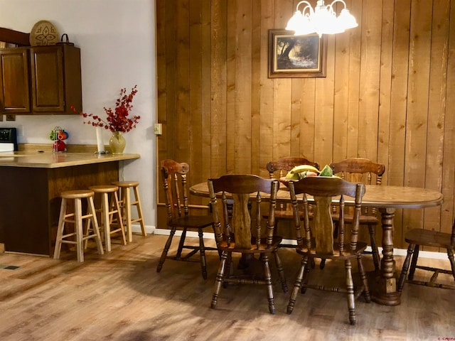 dining room featuring a chandelier, bar area, light wood-type flooring, and wooden walls