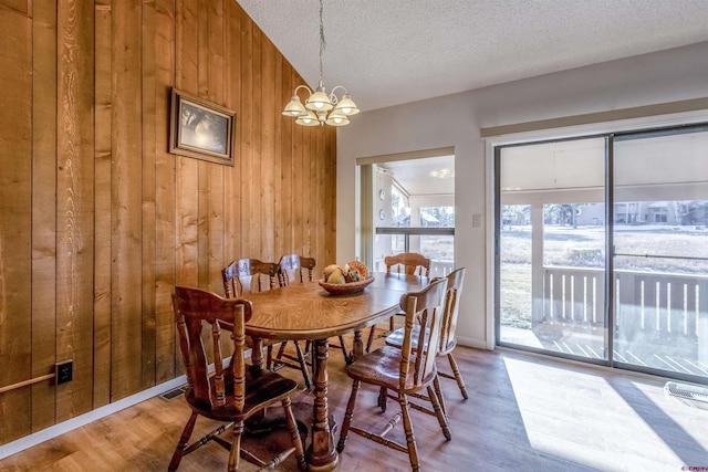 dining room with a chandelier, a textured ceiling, hardwood / wood-style flooring, and wooden walls