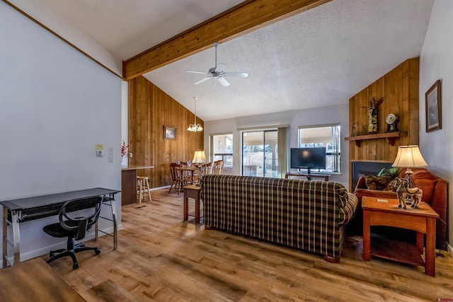 living room with lofted ceiling with beams, ceiling fan with notable chandelier, wooden walls, a textured ceiling, and wood-type flooring