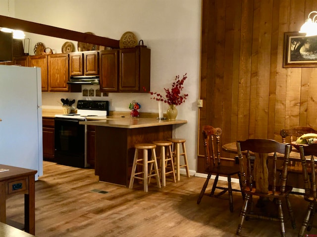 kitchen featuring a breakfast bar, white appliances, wooden walls, light wood-type flooring, and kitchen peninsula