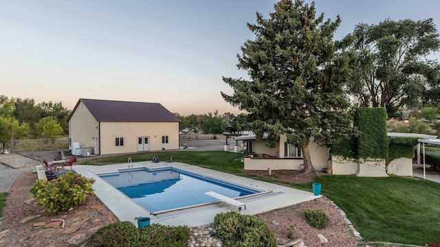 pool at dusk with a yard, a diving board, and a patio