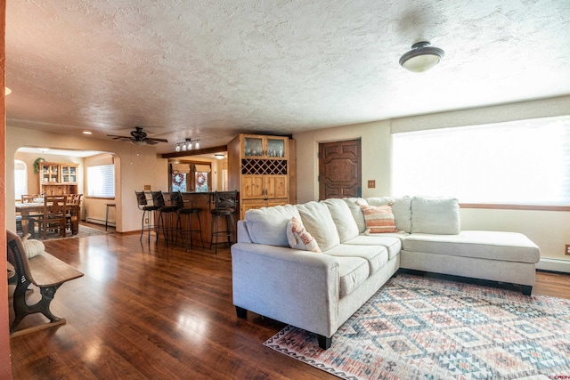 living room featuring dark hardwood / wood-style floors, a textured ceiling, a baseboard heating unit, and ceiling fan