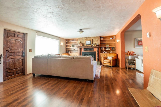 living room featuring a stone fireplace, a textured ceiling, dark hardwood / wood-style floors, and built in shelves