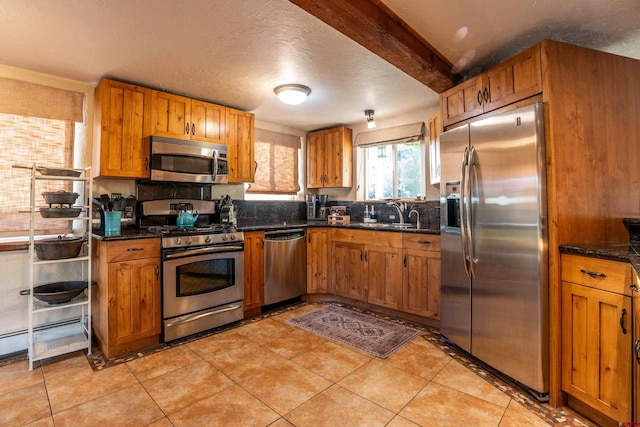 kitchen featuring appliances with stainless steel finishes, sink, light tile patterned flooring, a textured ceiling, and dark stone countertops