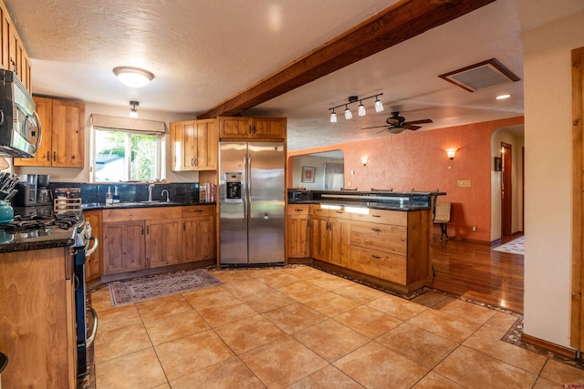 kitchen featuring a textured ceiling, kitchen peninsula, ceiling fan, stainless steel appliances, and beamed ceiling