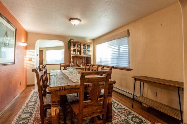 dining area featuring a baseboard radiator, wood-type flooring, and a textured ceiling