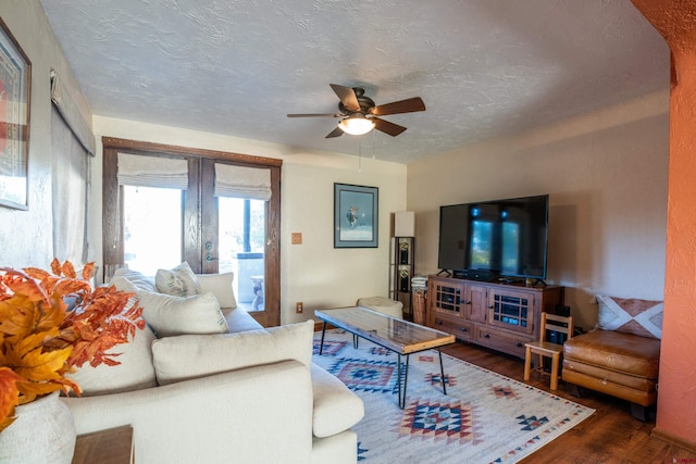 living room with a textured ceiling, dark wood-type flooring, and ceiling fan