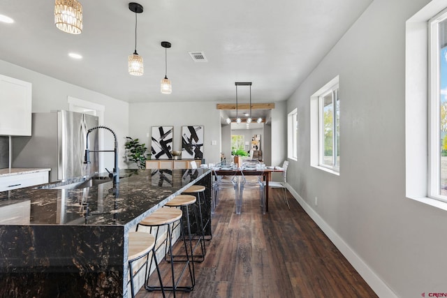 kitchen with a breakfast bar area, dark wood-type flooring, pendant lighting, and dark stone countertops