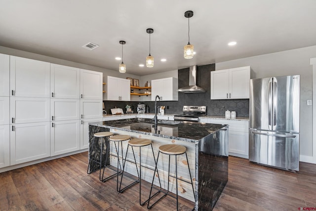 kitchen with a center island with sink, dark wood-type flooring, wall chimney range hood, and stainless steel appliances