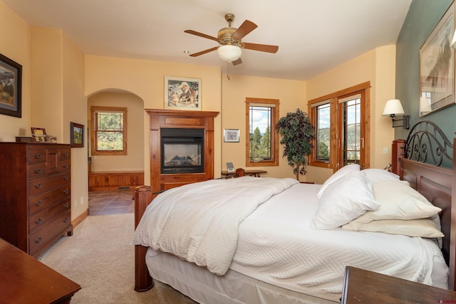 2239 Mockingbird Valley Ct, Durango, CO 81301 - bedroom featuring arched walkways, a glass covered fireplace, light carpet, ceiling fan, and ensuite bathroom