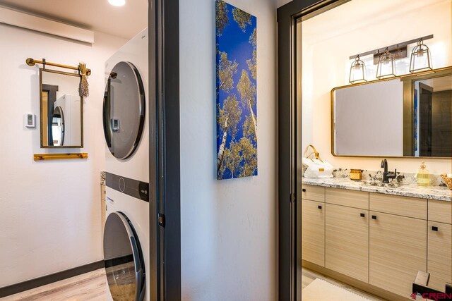 washroom with sink, an AC wall unit, light hardwood / wood-style flooring, and stacked washer and clothes dryer