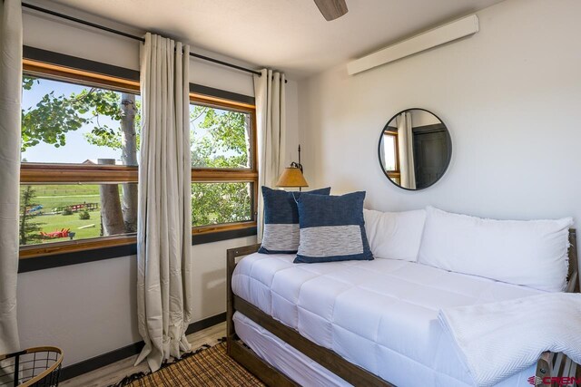 bedroom featuring ceiling fan, an AC wall unit, wood-type flooring, and multiple windows