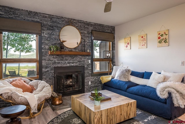 living room with a healthy amount of sunlight, ceiling fan, a stone fireplace, and wood-type flooring