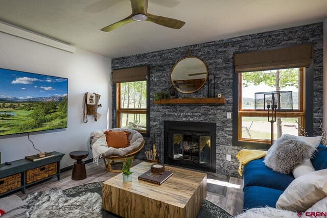 living room featuring a stone fireplace, wood-type flooring, and ceiling fan