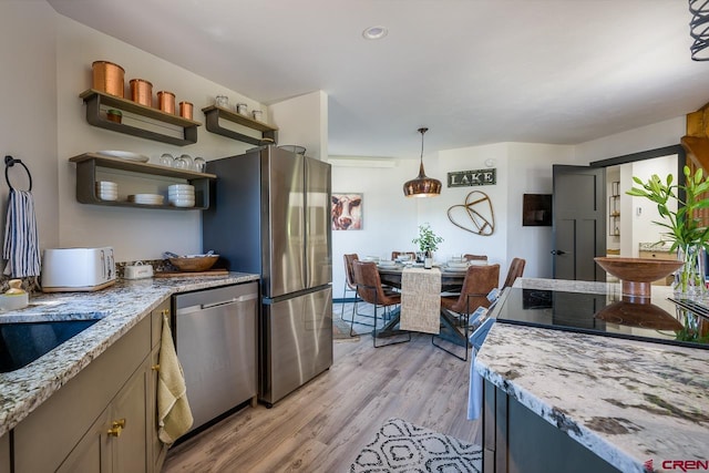 kitchen with appliances with stainless steel finishes, light stone countertops, pendant lighting, light hardwood / wood-style floors, and sink