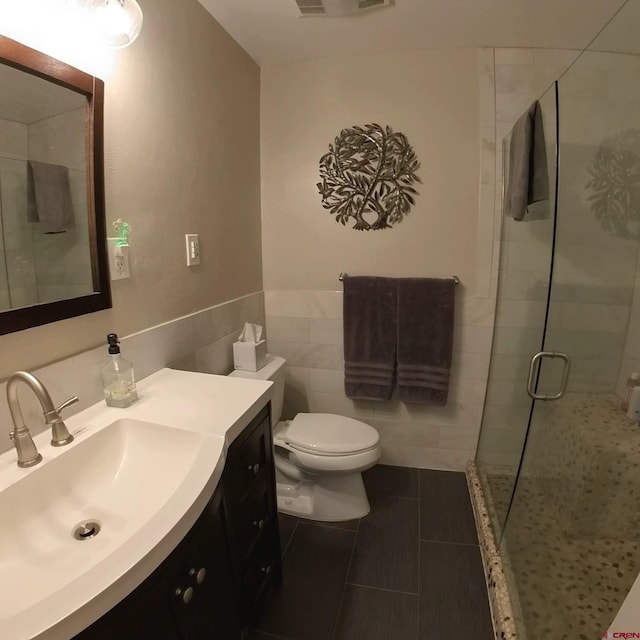 bathroom featuring tile patterned floors, toilet, vanity, tile walls, and an enclosed shower