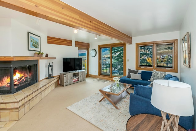 carpeted living room featuring beamed ceiling and a tiled fireplace