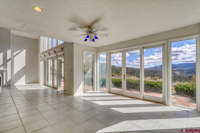 unfurnished sunroom featuring ceiling fan, a mountain view, and plenty of natural light