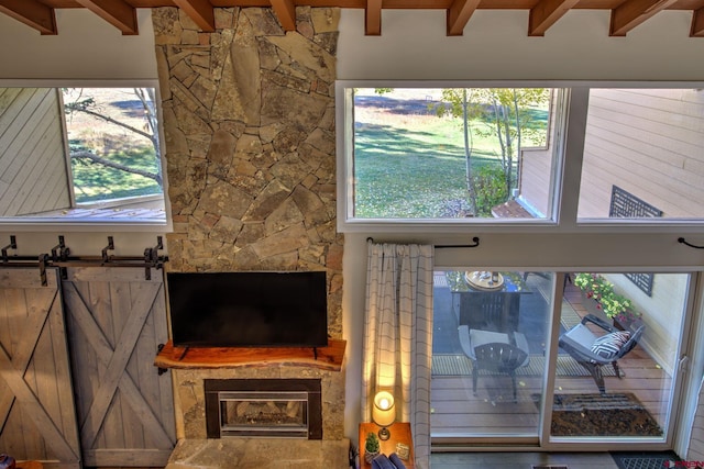 living room featuring beam ceiling, a barn door, and a stone fireplace