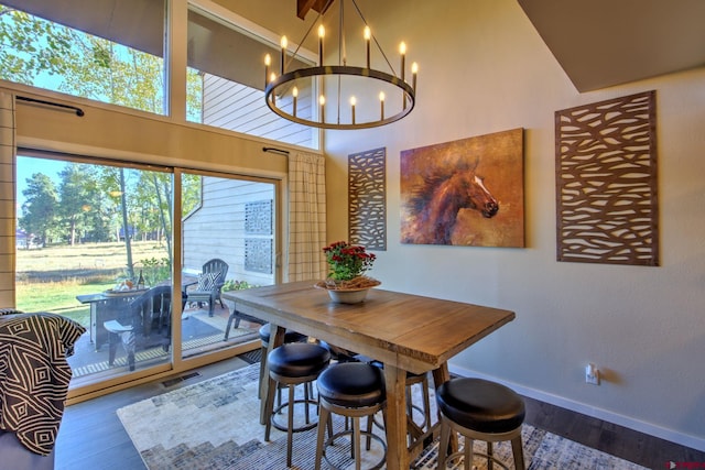 dining area featuring a towering ceiling, wood-type flooring, and an inviting chandelier